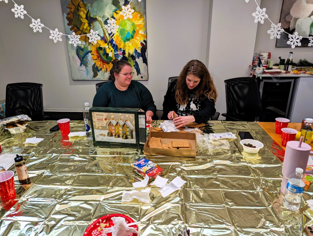 Two people sitting at a table building a gingerbread man.